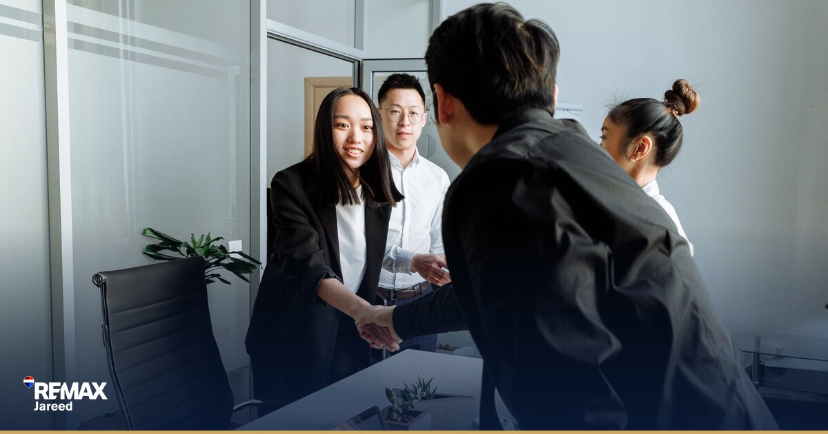 Two professionals shaking hands across a desk during a property negotiation meeting in a modern office setting