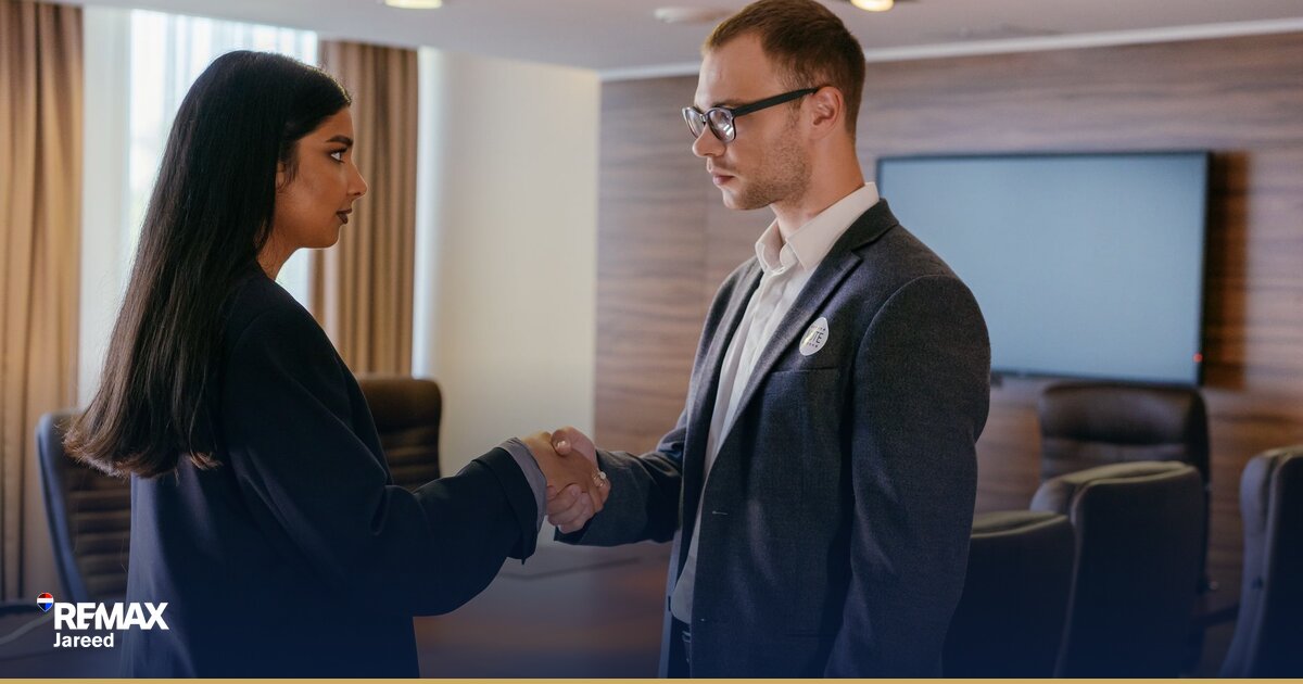 Two professionals shaking hands across a table during a property negotiation meeting in a modern office