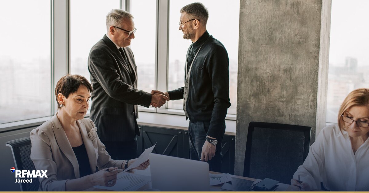 Two professionals shaking hands across a negotiation table with property documents in Sheikh Zayed real estate transaction