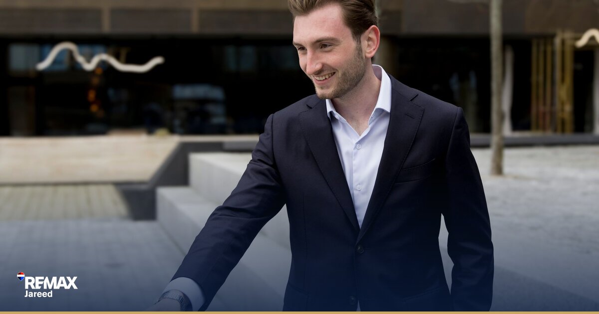 Two professionals shaking hands over signed property sale contract on modern desk