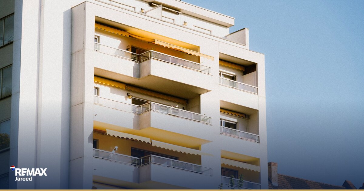 يد تُوَقِّع عقد شراء عقاري على مكتب مع مستندات ومخططات معمارية