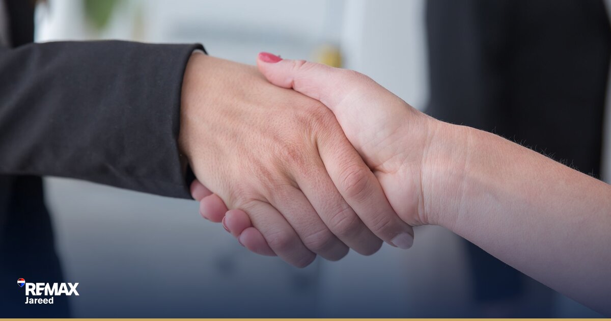 Two professionals shaking hands over a real estate contract during a successful property negotiation meeting in a modern office setting