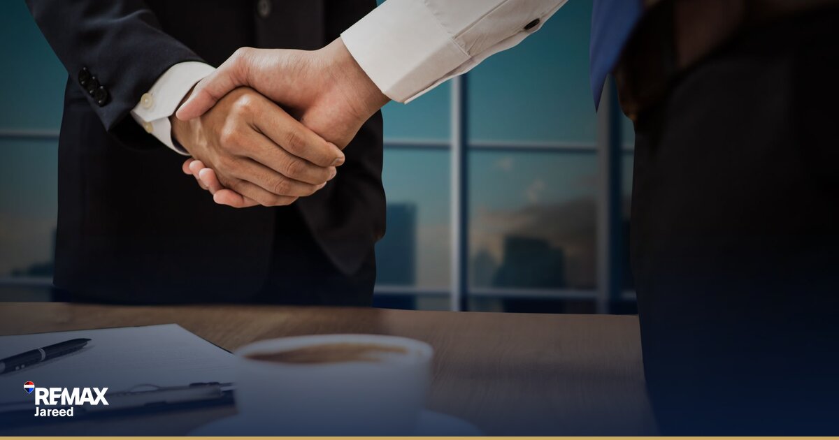 Two professionals shaking hands across a desk during property negotiation meeting